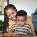 Loving mother reading to her cute little son while sitting together in their living room at home